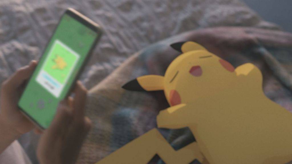 A sleepy Pikachu, with a person holding up a phone using the Pokemon Sleep app